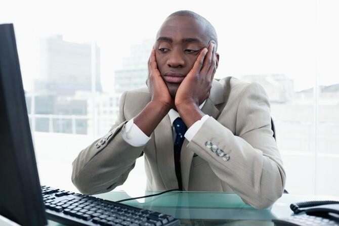 Bored zakenman die zijn computer in zijn bureau bekijkt