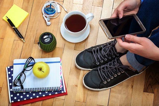 Persoon met smartphone, kopje koffie, notebook etc.