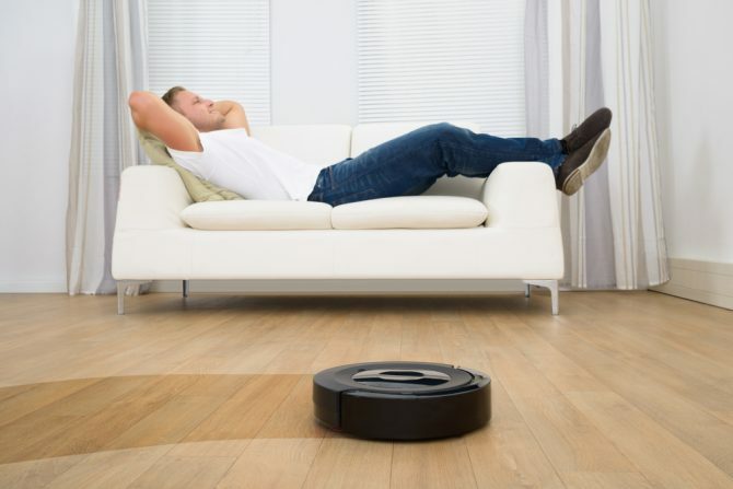 Man ontspannen op de sofa met robot stofzuiger op hardhouten vloer
